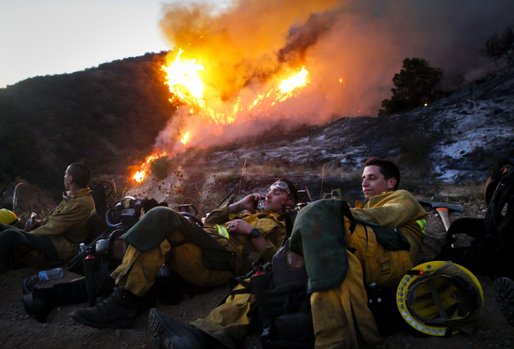 Camp 8 brush fire squad members take a break as a valley catches fire in Duarte, California on June 20, 2016. As temperatures reached triple digits, more than 1,000 firefighters deployed to fight two fires that raged just miles apart from each other in Duarte and Azusa, California.. Together, the fires burned around 5,000 acres and forced the evacuation of at least 770 homes according to the Los Angeles County Fire Department.