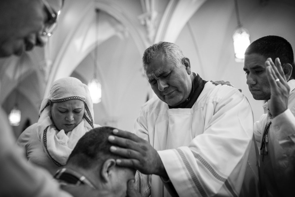 A man cries on the altar of St. Joseph's Church as Spanish-speaking members of the congregation lay hands on and pray for him during the Adoration of the Blessed Sacrament on Saturday, Oct. 8, 2016. | Photo by Gabriel Scarlett