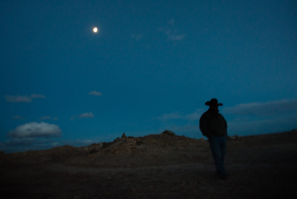 Larry Gordy walks among the testing pits and waste mounds on his grazing lands on the Navajo Nation near Cameron, Arizona. He remembers trail riding with his father, a Navajo uranium miner across this poisoned land before his death.
